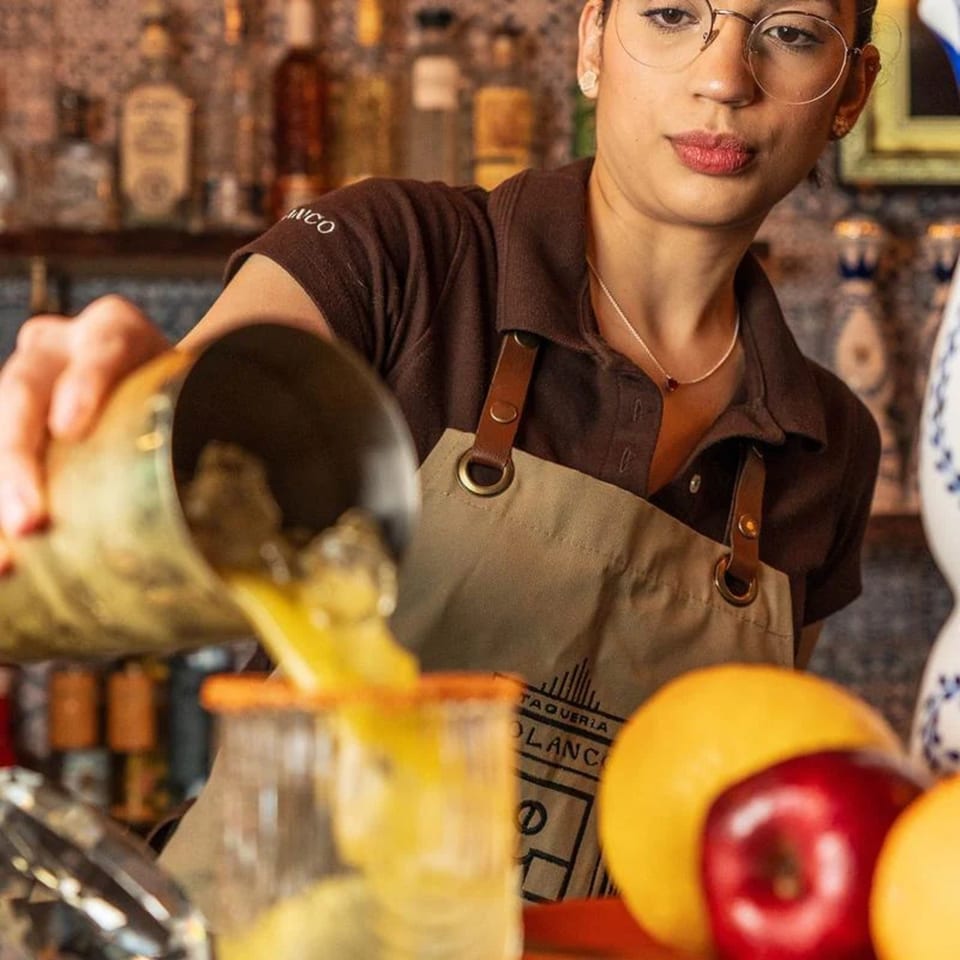 A Polanco Taqueria bartender pours a yellow drink from a shaker into a glass.
