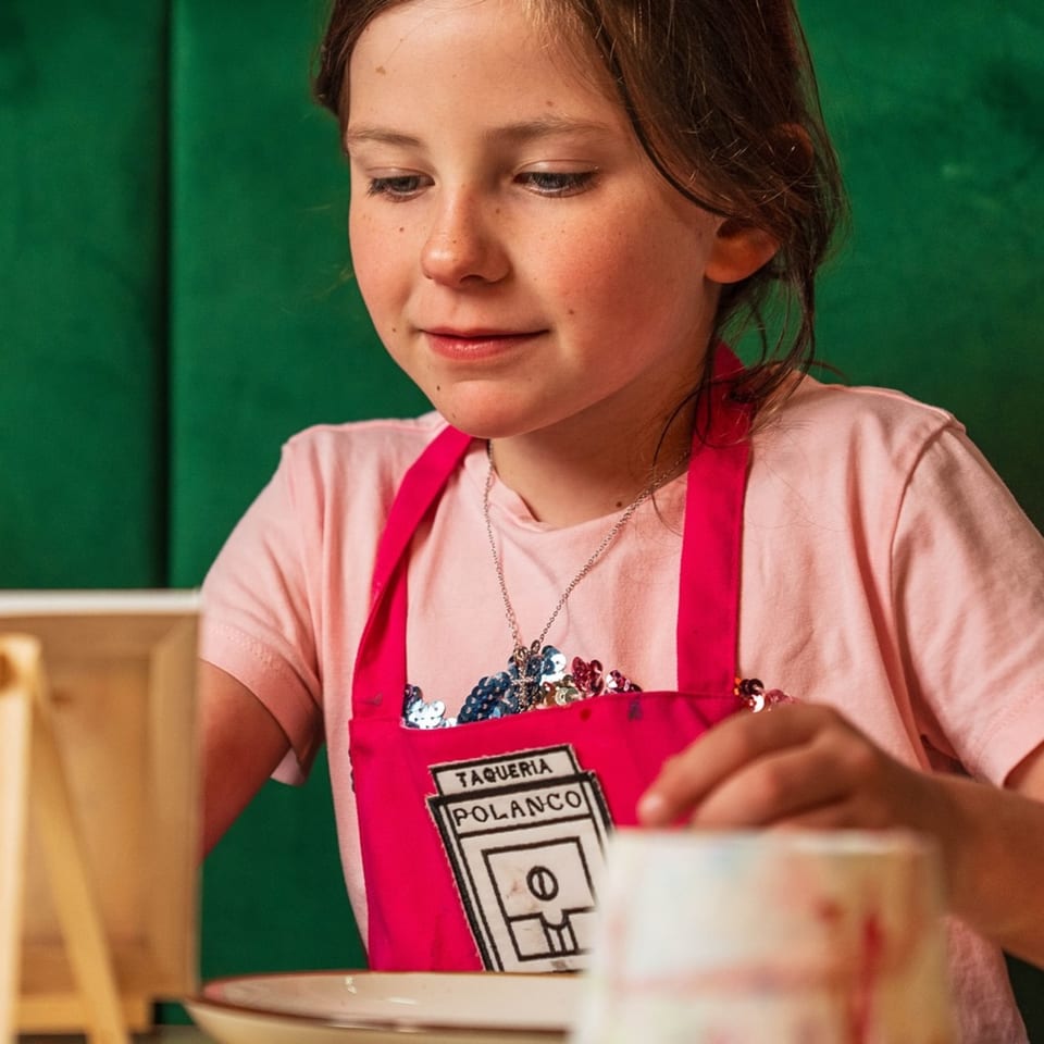 Young girl in a pink Polanco Taqueria apron looking down, engaged in an activity.