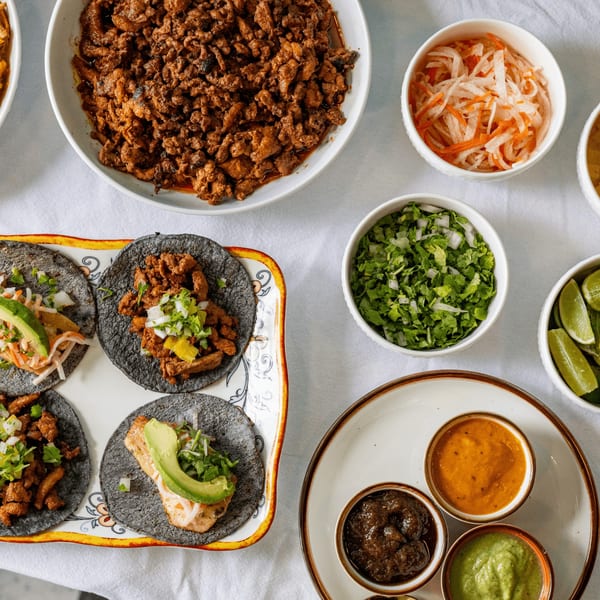 Overhead view of Polanco Taqueria's Mexican tacos, various toppings, and sauces on a white table.