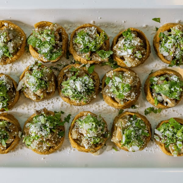 Rows of Mexican sopes topped with meat, cilantro, onions, and cotija cheese on a white platter.