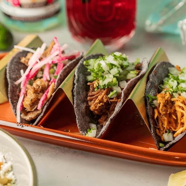Three Polanco Taqueria tacos with blue corn tortillas, various fillings, and toppings on an orange tray.