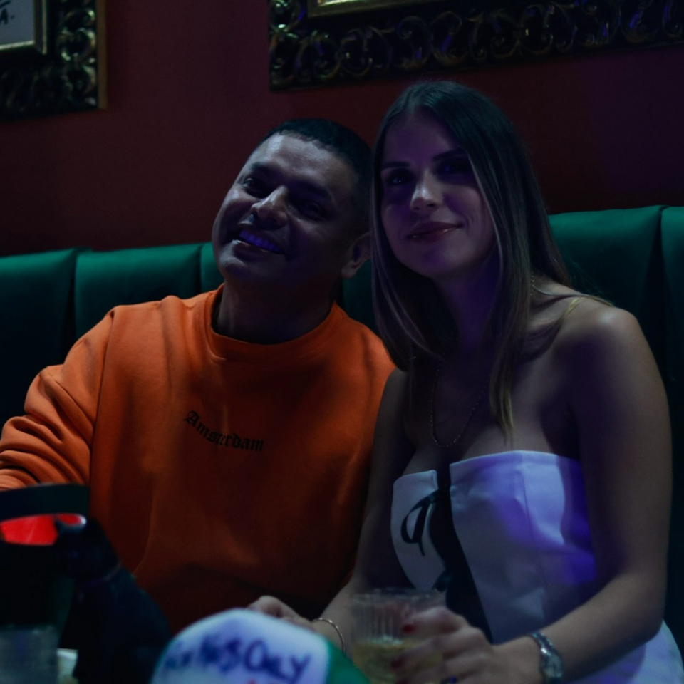 Two patrons, a man and a woman, smiling while seated in a dimly lit restaurant booth.