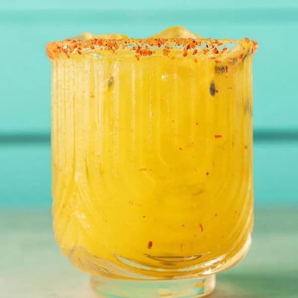 Close-up of a vibrant yellow Polanco Taqueria drink with a chili-salted rim against a blue background.