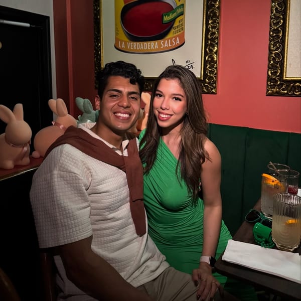 Smiling couple at Polanco Taqueria, with drinks and a salsa poster in the background.